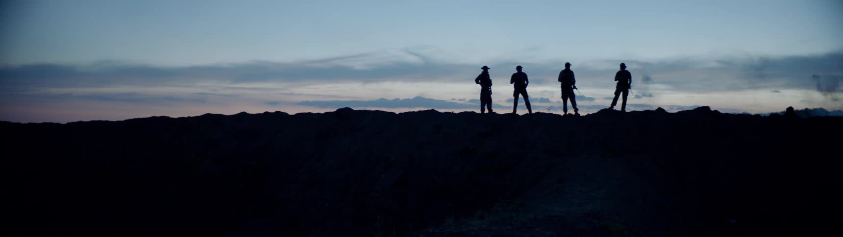 Men holding rifles are standing on the horizon after sunset