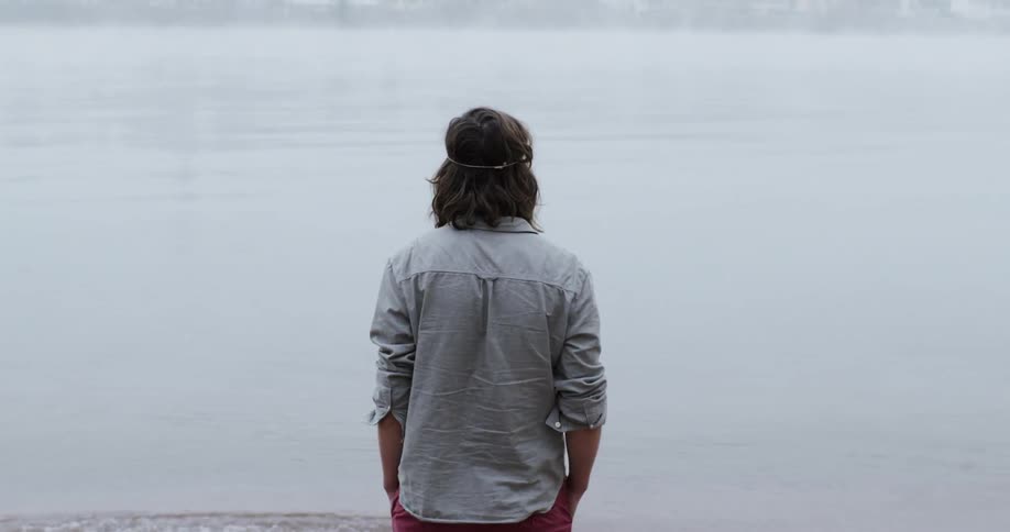 A man with hands in his pockets walks toward the water