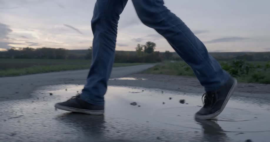 A man walks over a puddle on the trail
