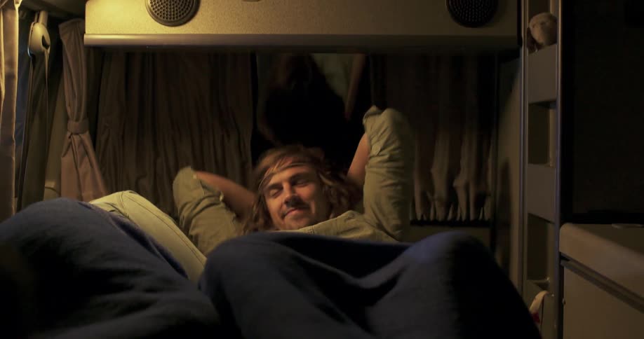 A man lays down next to another person in a camper