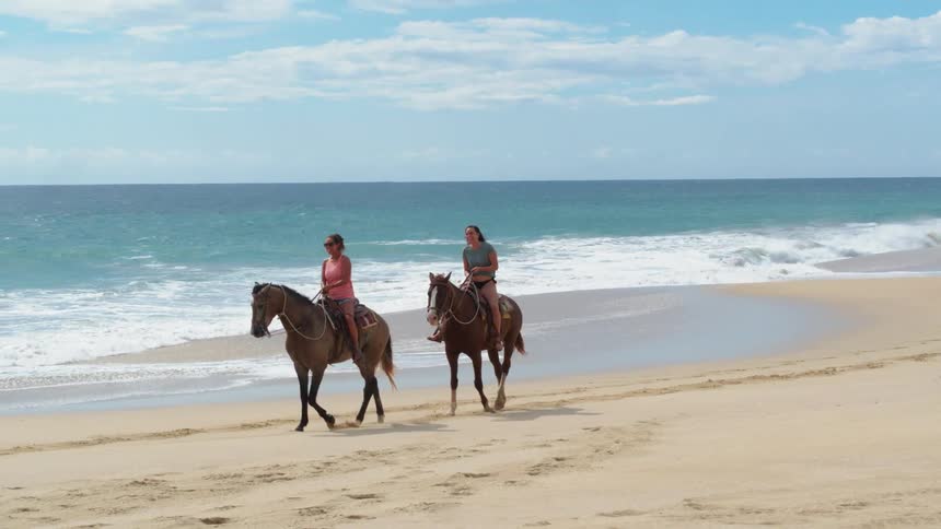 Women ride horses along the beach