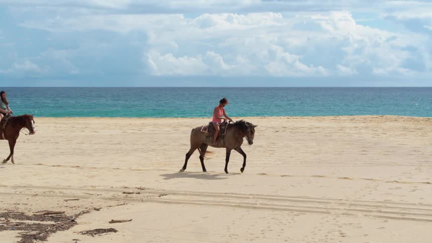 Two women ride horses on the beach