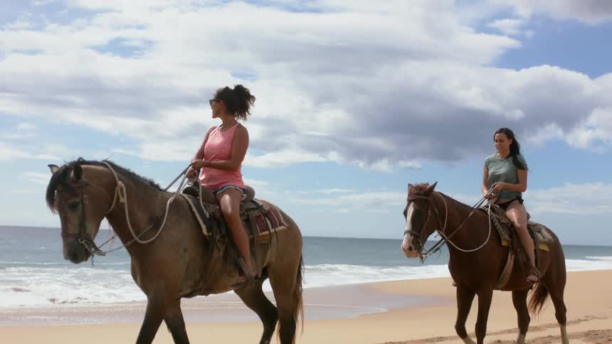 Two women ride horses on the beach