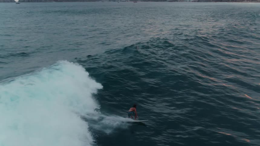 Man surfs on an ocean wave at sunset