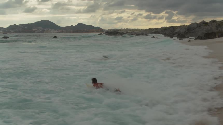 A surfer carries his surfboard and dives into the water