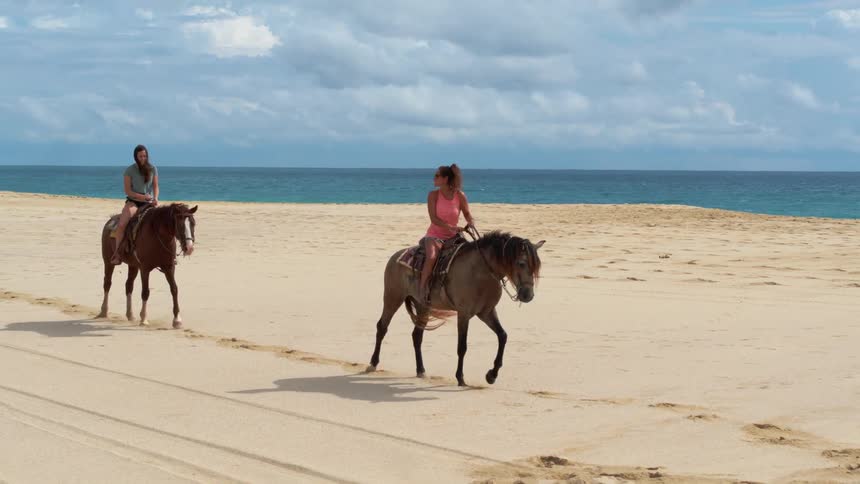 People ride their horses on the sand