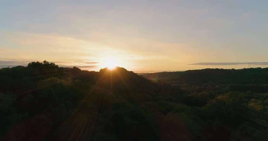 The sun shines over the hills by the water