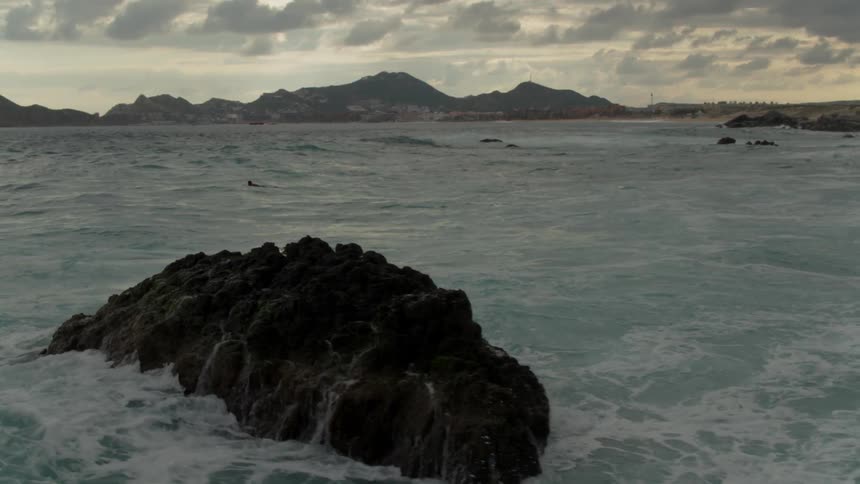 Ocean waves crash into a rock at sunset