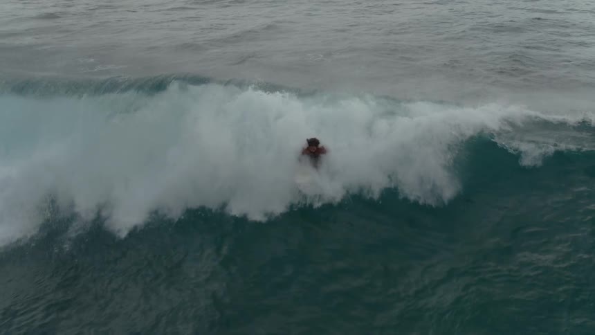 A surfer paddles in front of a wave and rides it