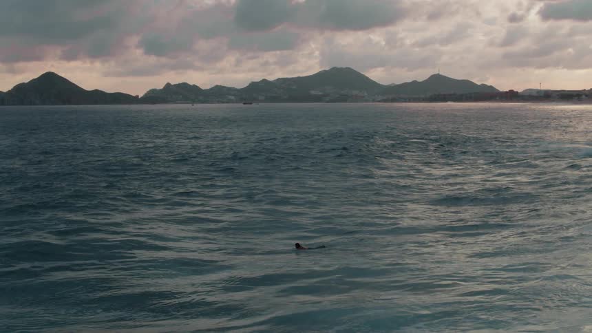 Person paddles on a surfboard at sunset