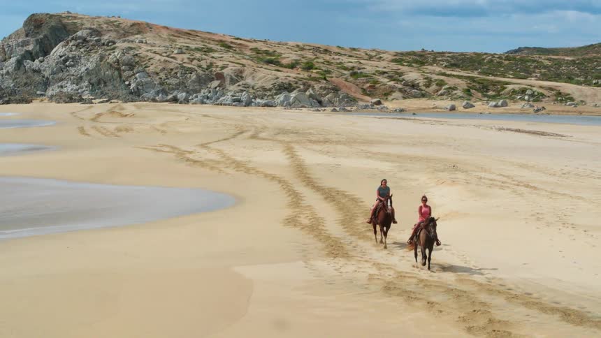 Two women ride horses on the beach