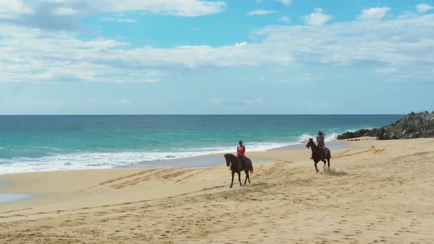 Two women ride horses on the beach
