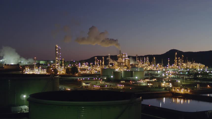 Flying low over petroleum refinery oil tanks at dusk
