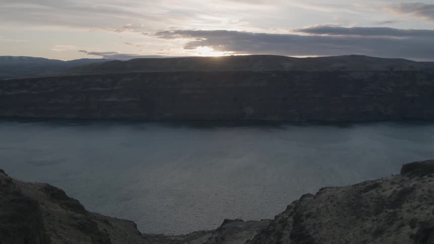 Flying off the edge of steep cliffs to reveal a deep river canyon as the sun sets in the distance