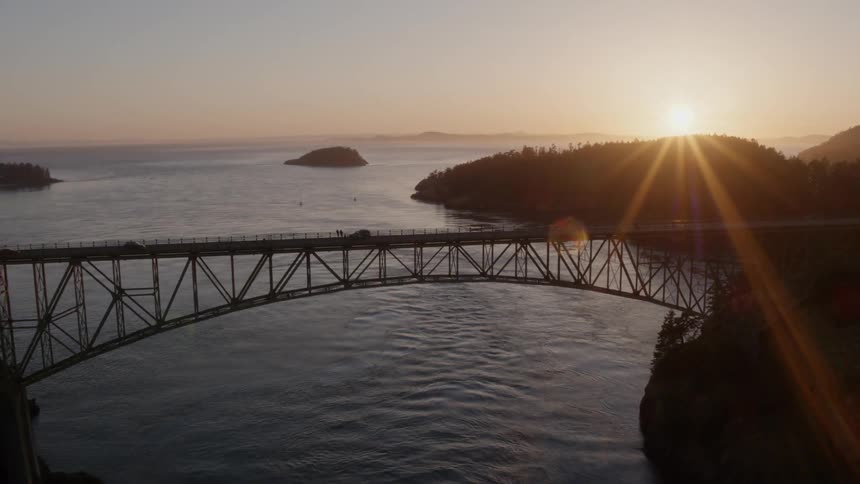 Pullback ascent reveal of a beautiful arched bridge high above rippled ocean water at sunset