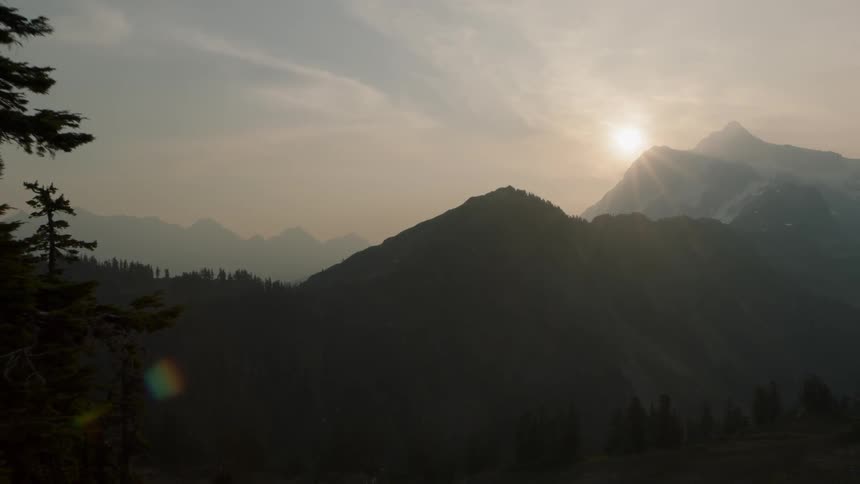 Revealing a small stand of alpine trees as the sun rises above rugged mountains in the distance