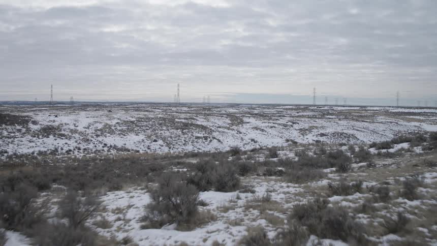 Tilt up reveal of power transmission lines crossing rural and snowy terrain