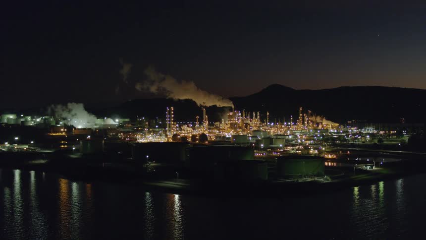 Oil refinery ascent at night over harbor water
