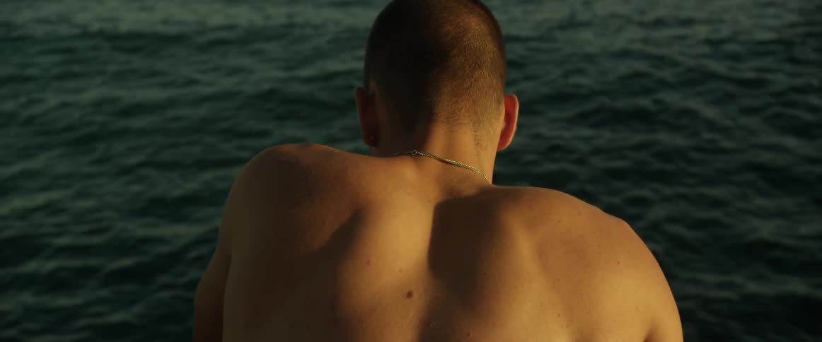 A shirtless man stands and looks down at the water