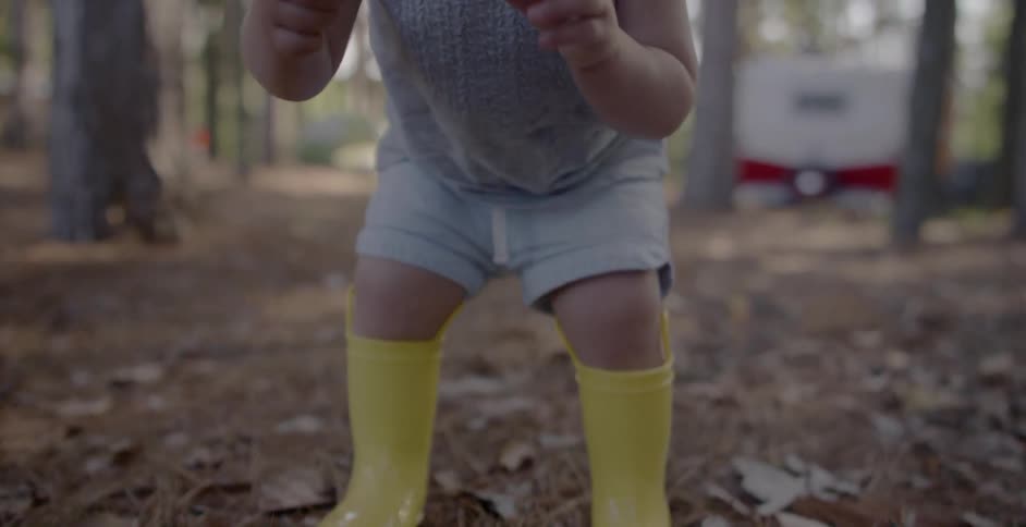 A toddler in yellow boots picks up a seed pod