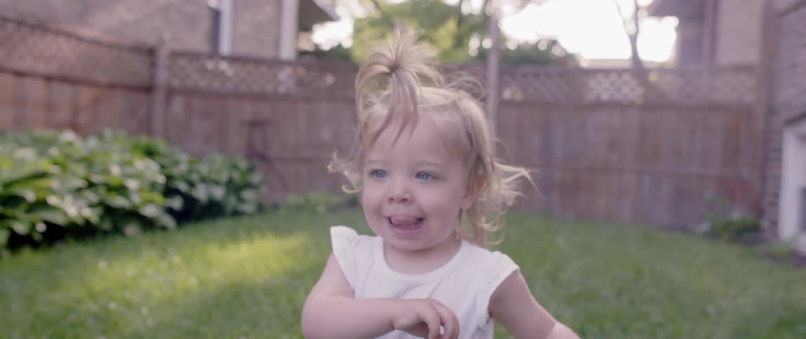 Toddler girl walks in a grassy backyard