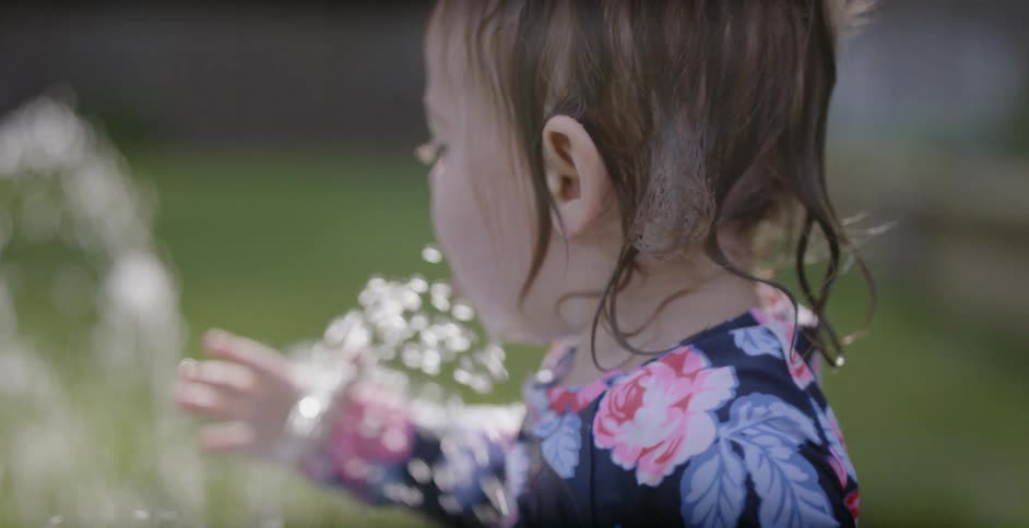 A child is having fun in the yard getting wet in the fountain