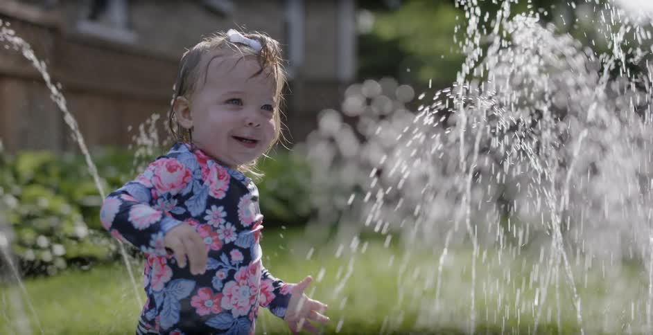 A young girl plays in a yard sprinkler