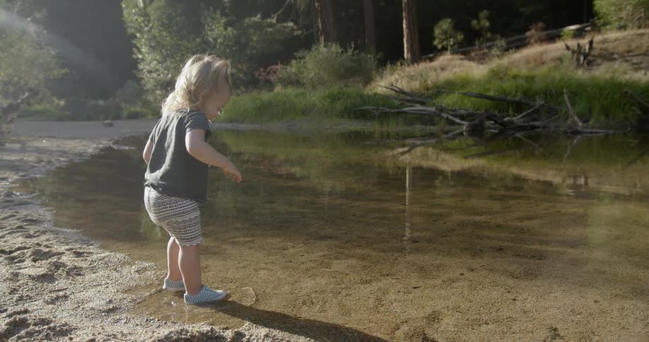 A girl walks into a shallow pond on a sunny day