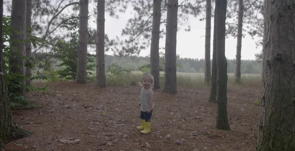 A child in boots stands by the trees and walks forward