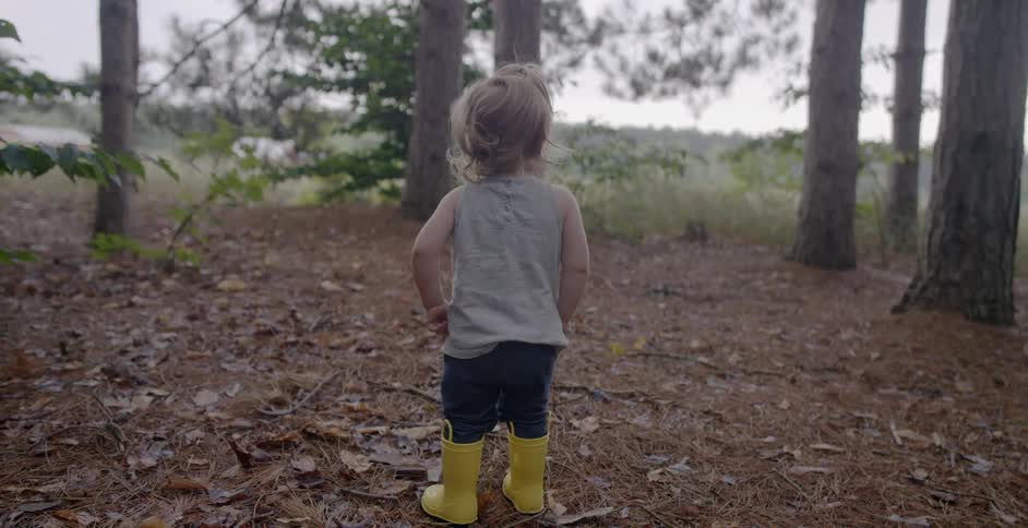 A child in yellow boots looks around the forest
