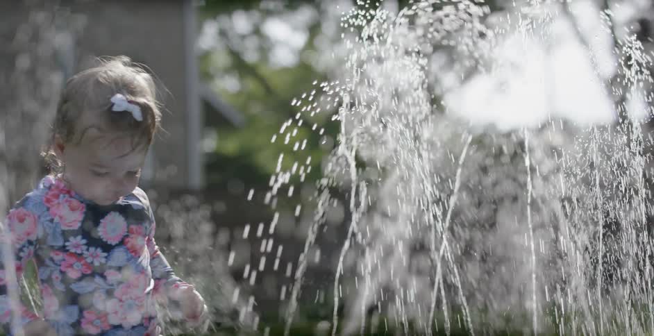 A toddler girl is playing in a water in a backyard during the day