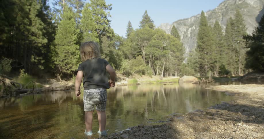 A toddler steps into a pond