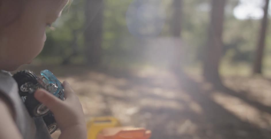 A child is sitting in the sun playing with toy trucks