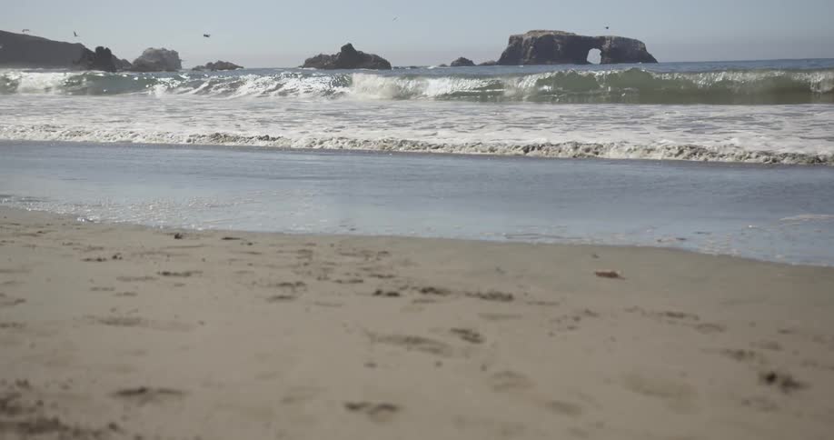 Ocean waves are rolling onto a beach on a sunny day