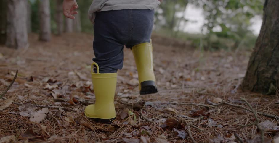 A child in yellow rubber boots walks through the leaves
