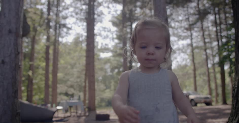 A toddler walks outside at a campsite in the woods