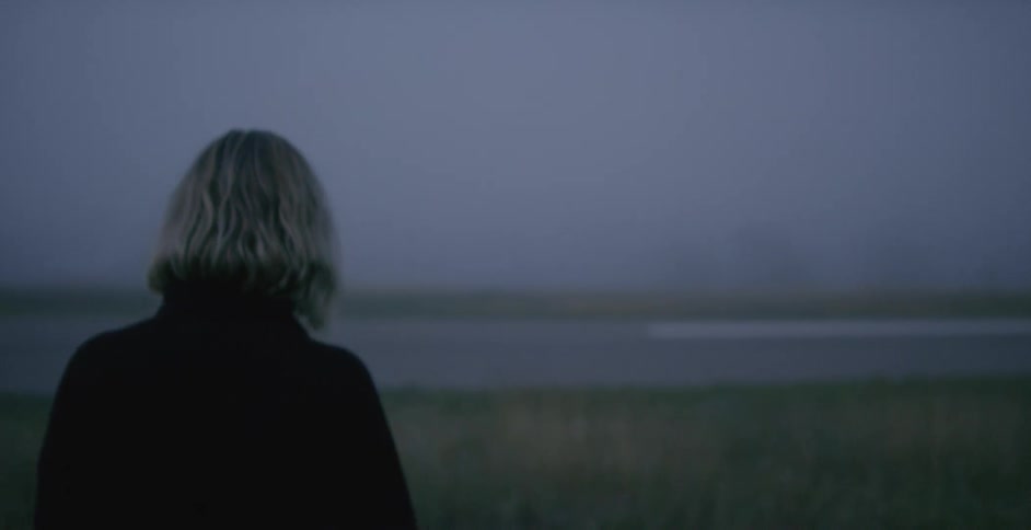 A woman is walking towards the water at sunset
