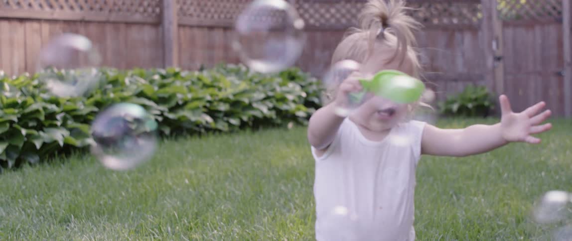 A toddler tries to catch bubbles outside