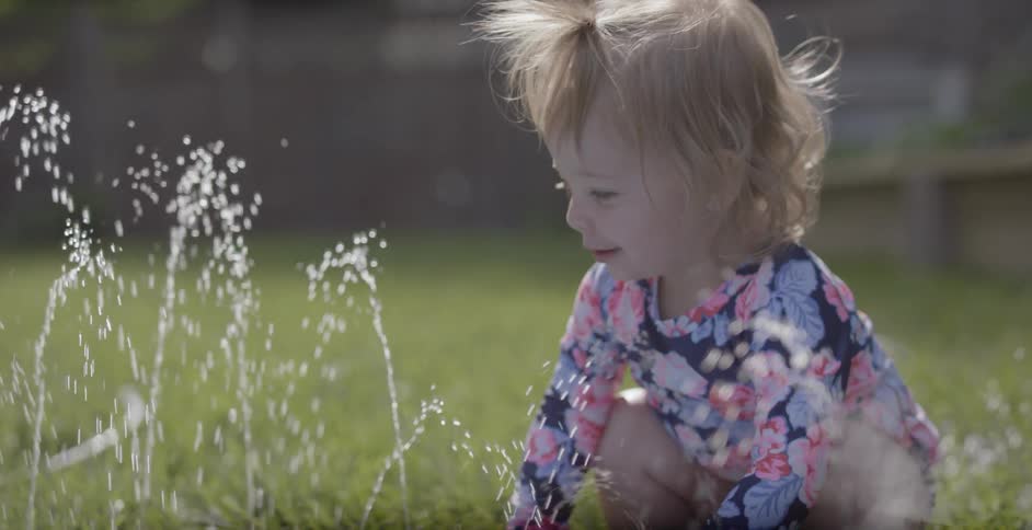 A toddler girl is playing in the water of a kiddie pool on a sunny day