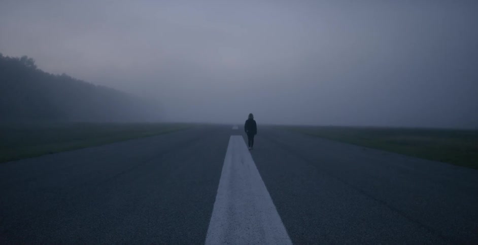 A woman walks down a desolate road through the fog