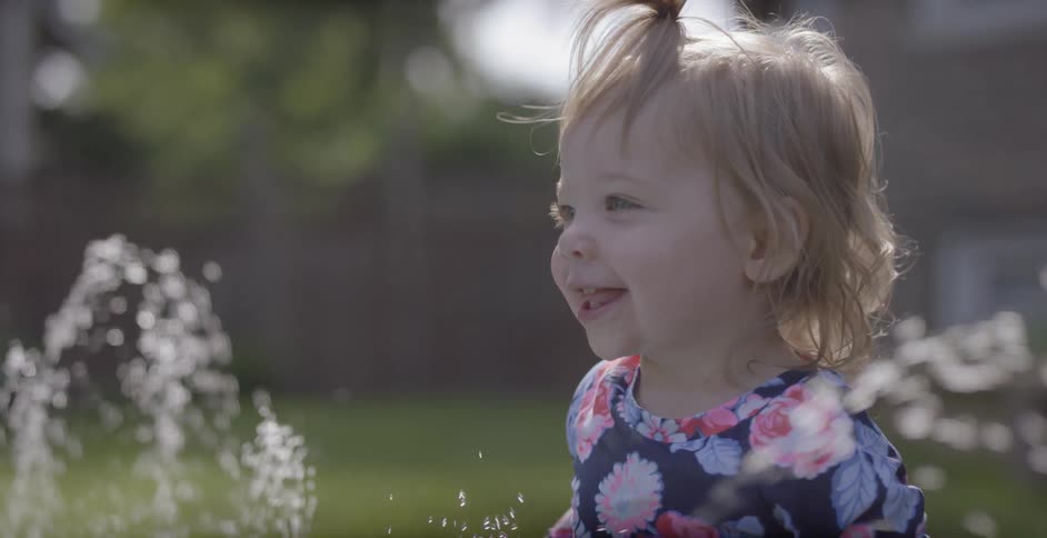 A toddler smiles while playing in water in a yard