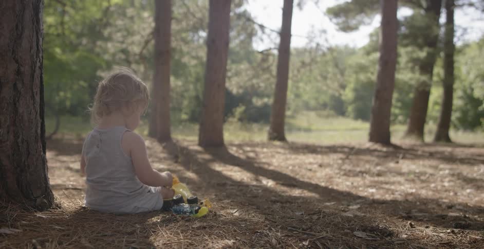 A child is sitting by a tree on a sunny day
