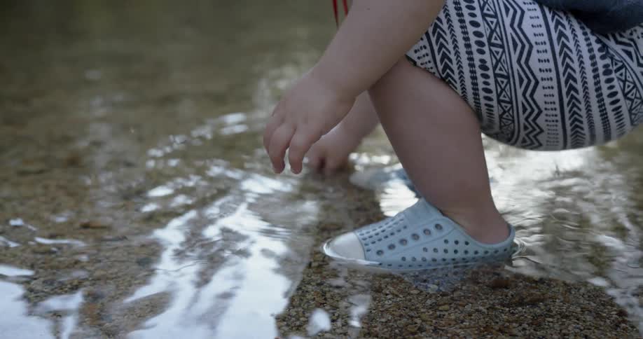 A little girl is squatting as she plays in a stream during the day