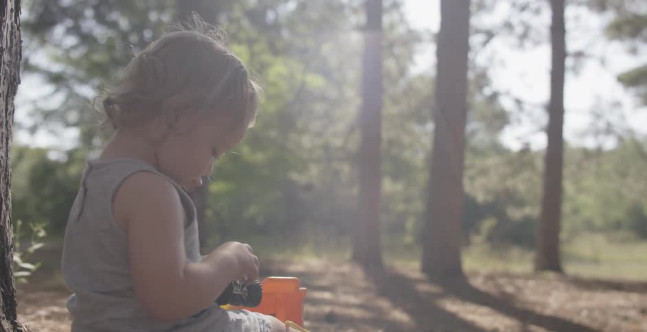 A toddler plays with toy cars in a forested area