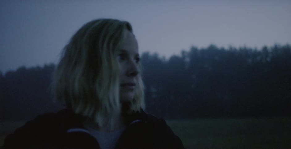 A woman looks worried in a rural field at dusk