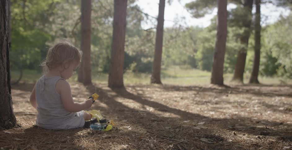 A toddler plays with toys while sitting in a forest