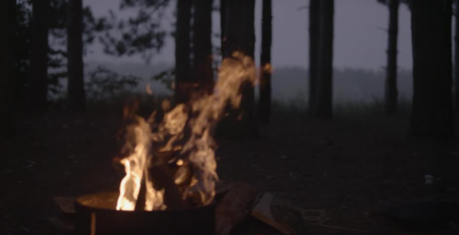 A camp fire burns in the woods at sunset