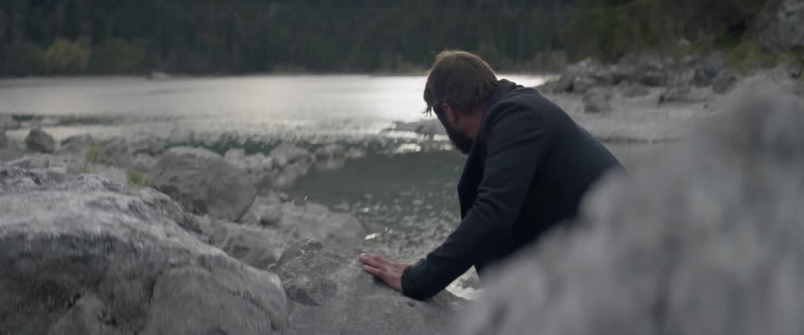 A man is leaning on the rocks by the lake