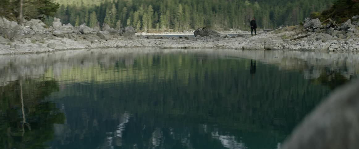A man hikes past the calm lake water