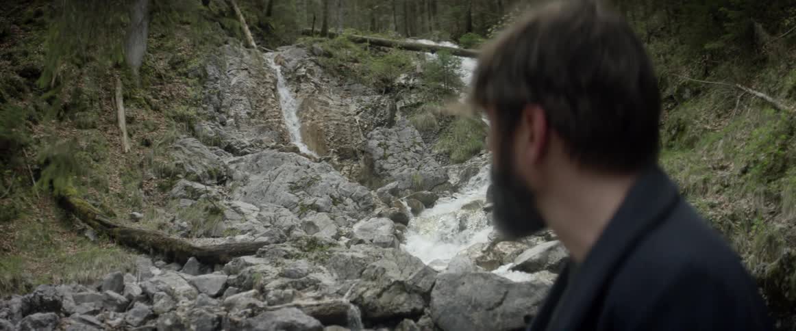 A bearded man stands by a small waterfall